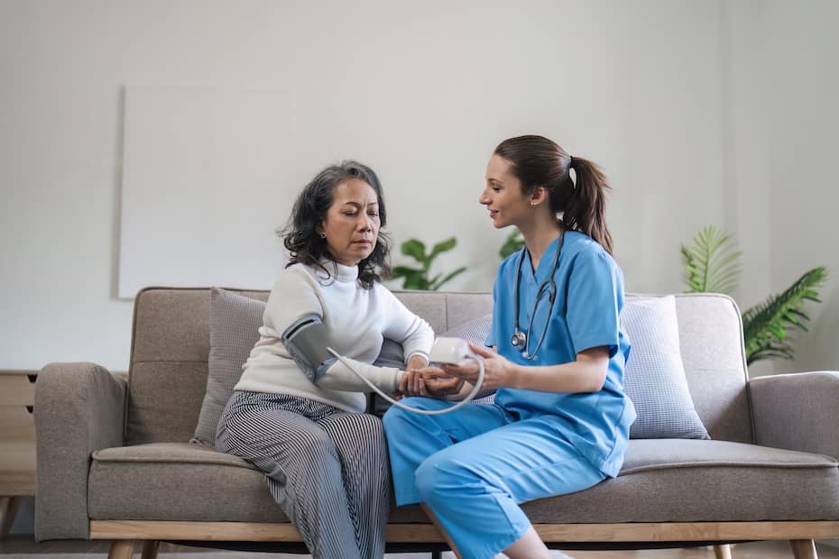 A healthcare professional in blue scrubs measuring the blood pressure of a senior woman at home, representing the role of an HHA in Chicago.