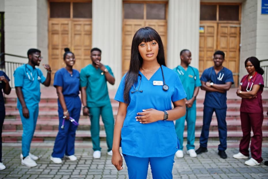 A group of healthcare students, including a young woman in blue scrubs, standing in front of a medical building in Chicago, representing CNA to LPN bridge programs.
