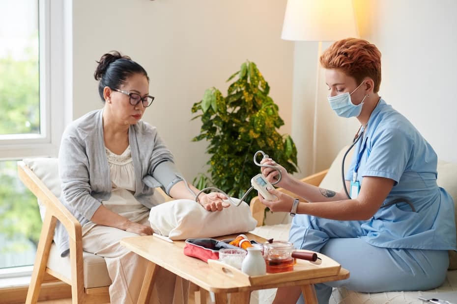A Patient Care Technician (PCT) checking a patient’s blood pressure at home during a routine health assessment.