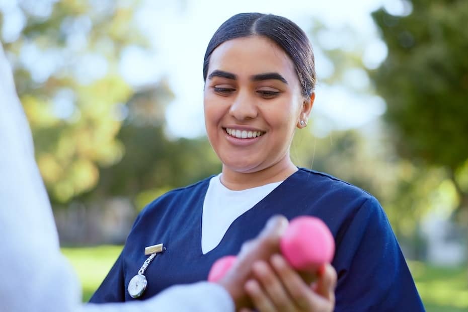A Registered Nurse (RN) in Chicago assisting a patient with light hand exercises using dumbbells during an outdoor rehabilitation session.